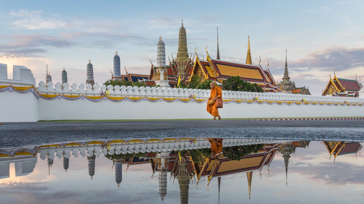 Monk walks in the morning after the rain in front of the Temple of the Emerald Buddha (Wat Phra Kaew), part of the Grand Palace, Bangkok, Thailand.
